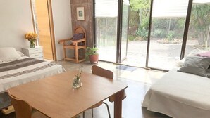 Habitación con cama, sofá, mesa de madera y una silla. Se ve follaje verde a través de la ventana.
