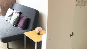 Una habitación con un sofá gris, una pequeña mesa de madera con un jarrón de flores, y una puerta con un letrero de advertencia.