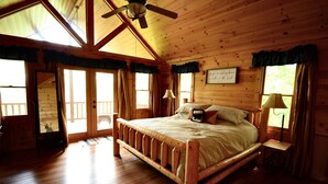 Een slaapkamer in een houten chalet met een groot bed, een plafondventilator en uitzicht op de omgeving.