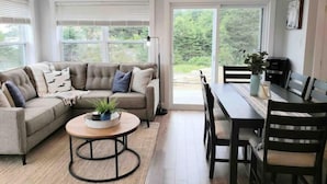 Una sala de estar moderna con un sofá modular, una mesa redonda de centro y un comedor con mesa y sillas.