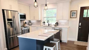 Una cocina moderna con electrodomésticos de acero inoxidable, una isla central con taburetes y un amplio ventanal que proporciona luz natural.