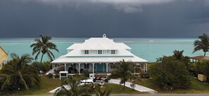Een wit gebouw met een overdekte veranda, omringd door palmbomen en uitzicht op de oceaan.