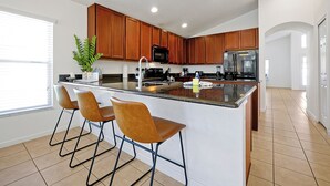 Una cocina moderna con armarios de madera, una isla central con taburetes de bar, un refrigerador de acero inoxidable y un amplio ventanal que proporciona luz natural.