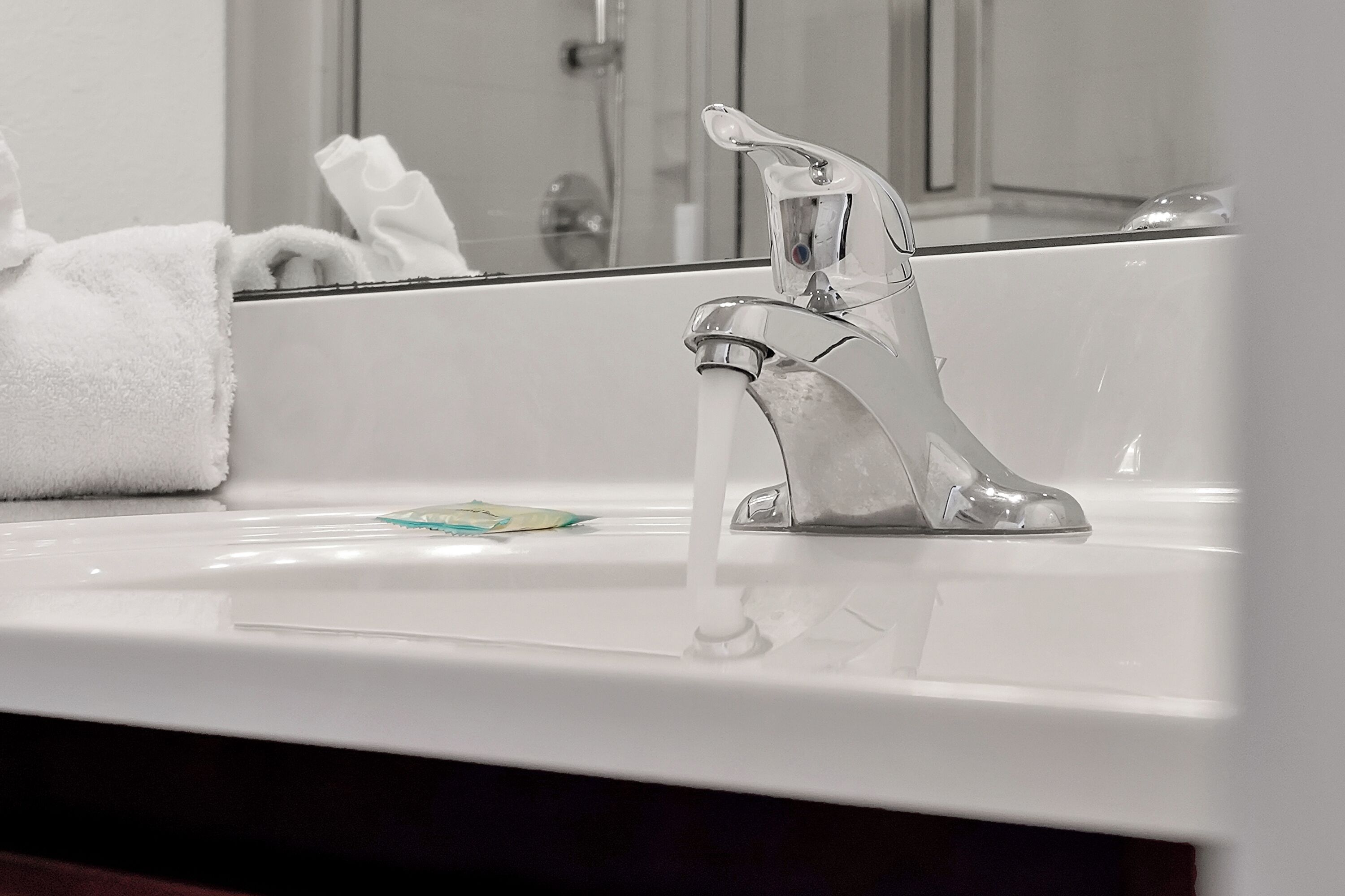 A bathroom sink with a modern faucet and a mirror reflecting a towel and a shower area.