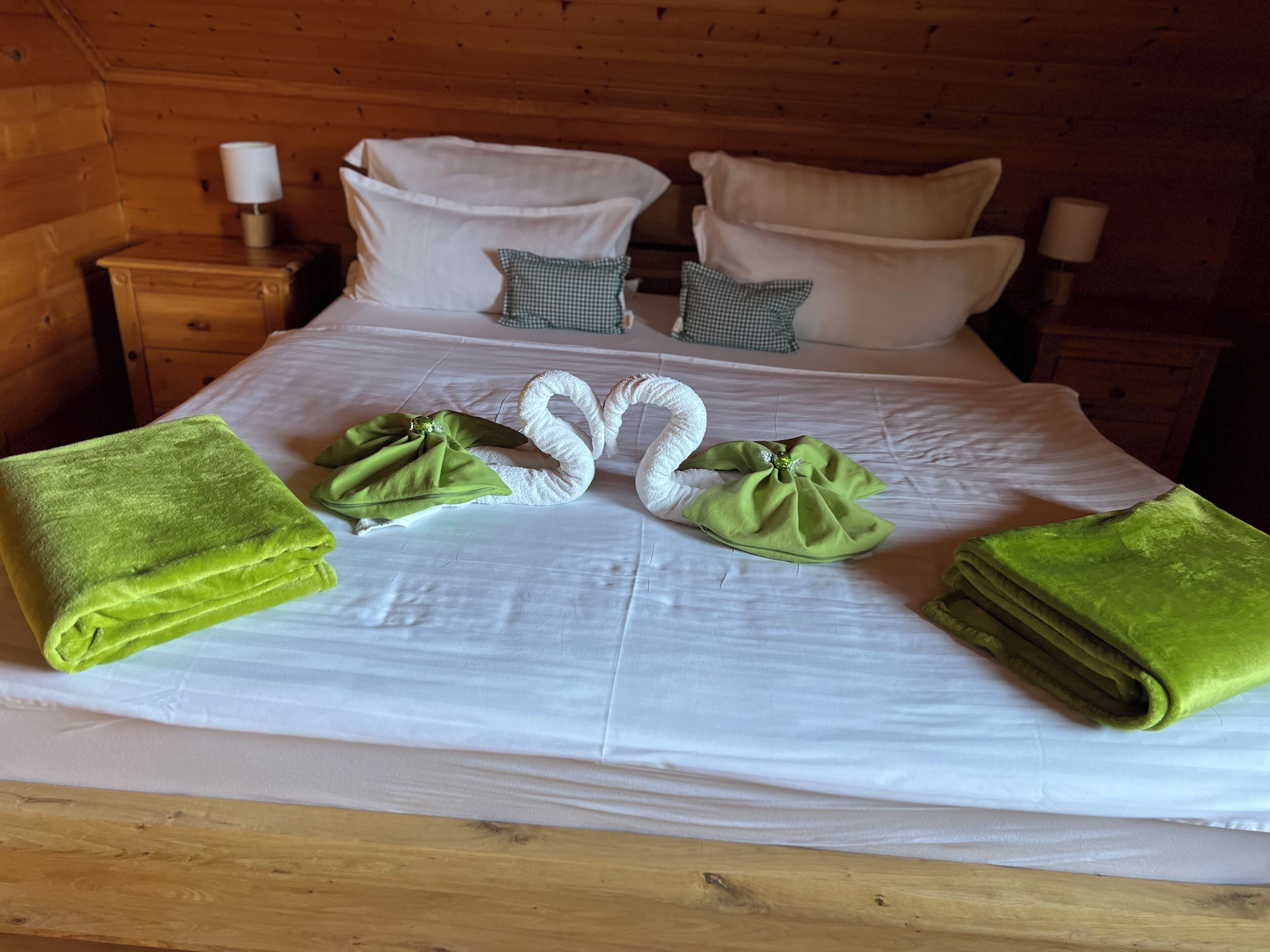 Ein ordentlich bezogenes Bett mit weißen Leinen und grün gefalteten Handtüchern in den Ecken.