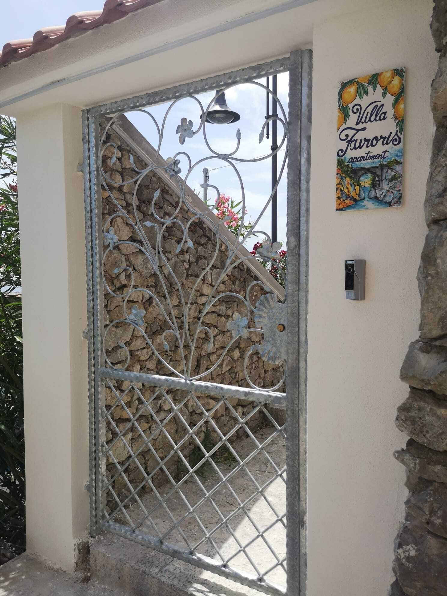 A metal gate with decorative patterns, a stone wall, and a sign that reads "Villa Auroris apartment".