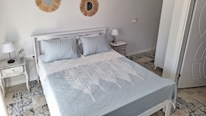 A bedroom with a bed, two bedside tables, a nightstand, a lamp, a mirror, and a door.