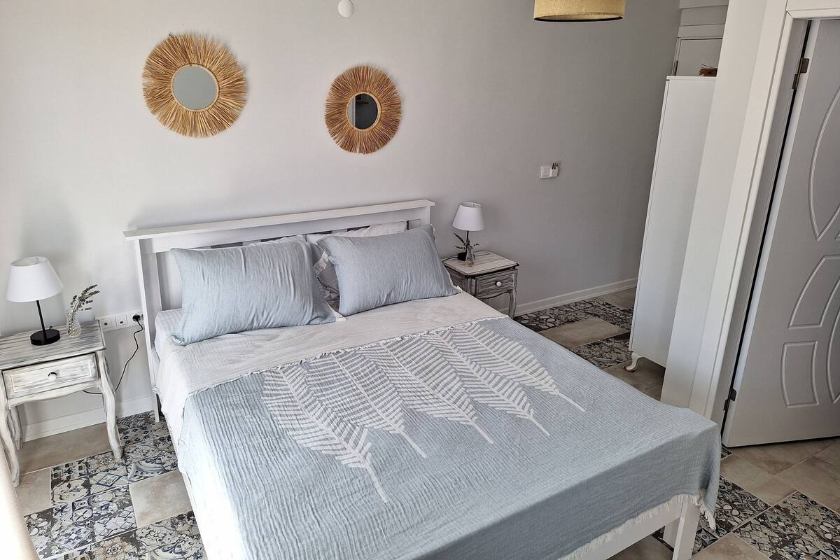 A bedroom with a bed, two bedside tables, a nightstand, a lamp, a mirror, and a door.