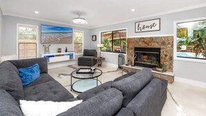 A modern living room with a grey sofa, a coffee table, a fireplace, and large windows offering a view of the outdoors. - Paradise in Clearwater (Clearwater)