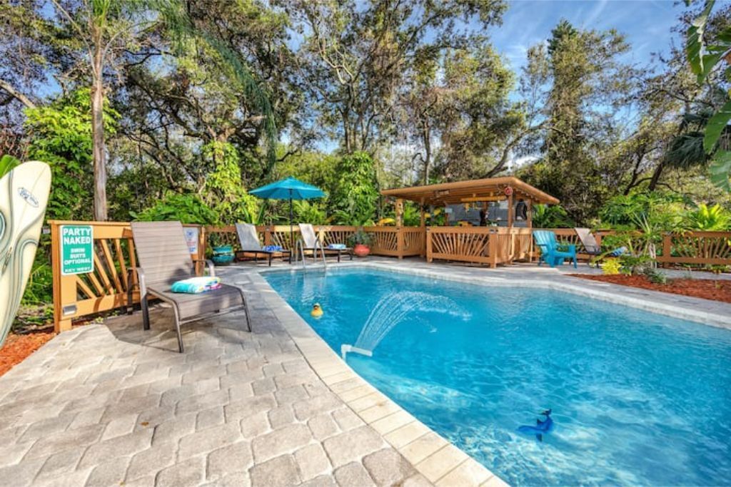A swimming pool with lounge chairs and a wooden gazebo, surrounded by trees.