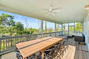A covered outdoor patio with a wooden table and chairs, a ceiling fan, and a view of trees and buildings. - Game room, swim spa, and more!, Game room, swim spa, and fun! (Gulf County)