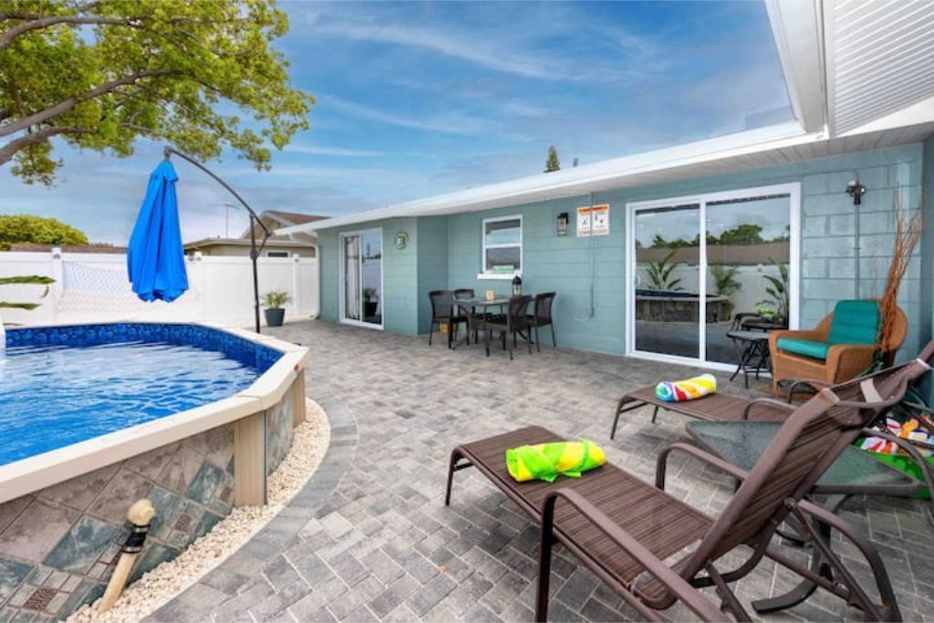 A backyard with a swimming pool, patio furniture, and a covered seating area.