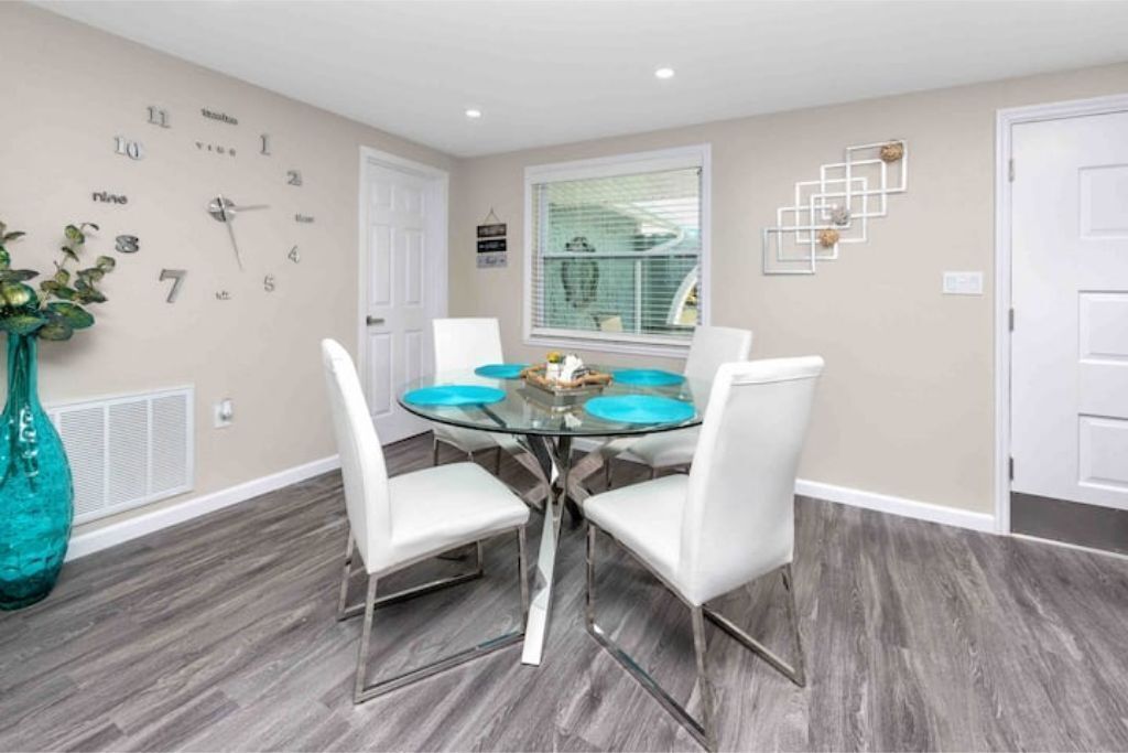 A dining area with a round glass table, white chairs, and a clock on the wall.