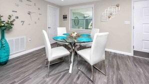 Un coin repas avec une table ronde en verre, des chaises blanches et une horloge au mur.