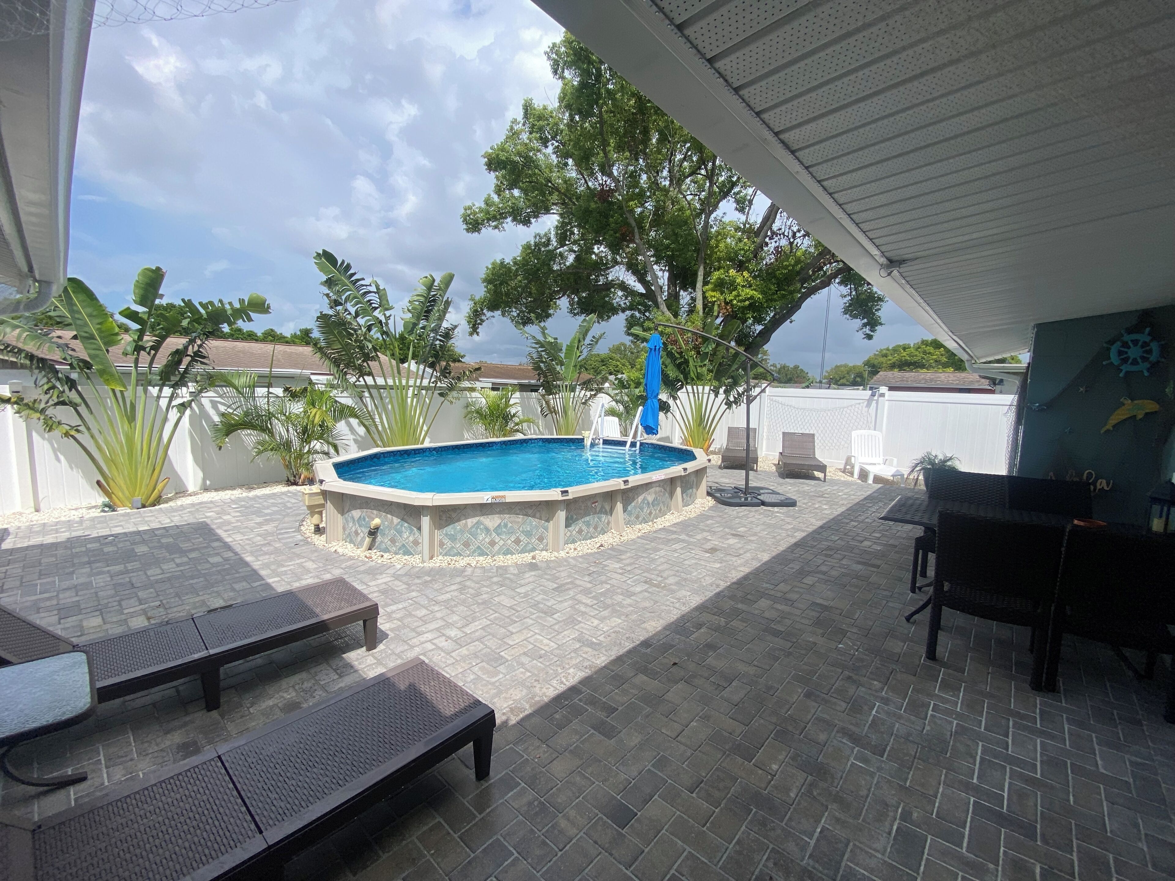A covered outdoor area with a swimming pool, lounge chairs, and a table.