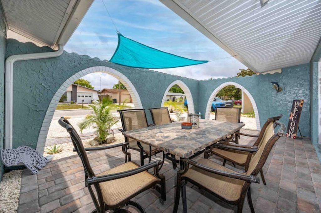 An outdoor patio with a table and chairs, a 'WELCOME' sign, and a view of the street through arches.