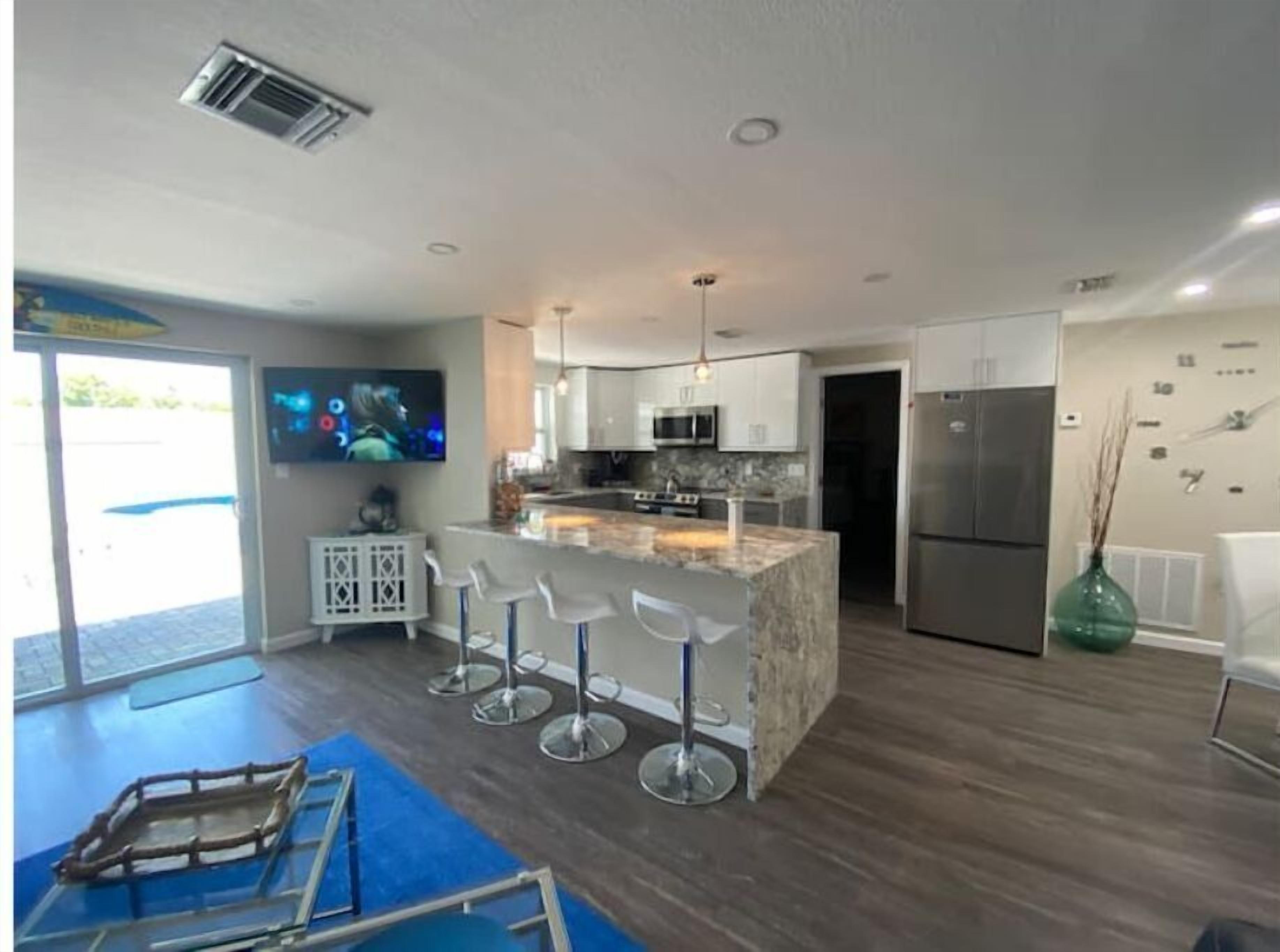 A modern kitchen with a central island, bar stools, stainless steel appliances, and a large window.