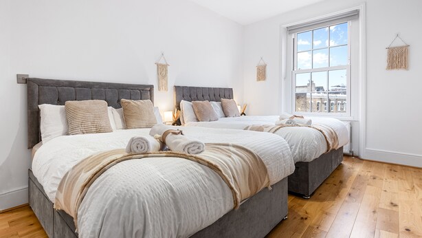 A modern bedroom with two beds, a large window, and a view of the city.
