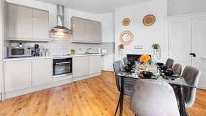 A modern kitchen with white cabinets, a stainless steel range hood, and a dining area with a glass table and grey chairs.