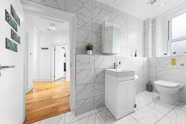 Une salle de bain moderne avec des carreaux de marbre blanc, un lavabo blanc et des toilettes.