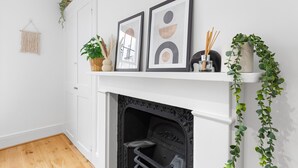 A white fireplace with a black surround, framed artwork above, and a hanging macrame wall hanging.