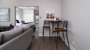 Un espace de vie moderne et compact, comprenant un canapé, une table à manger avec des chaises et un coin cuisine à l’arrière-plan.