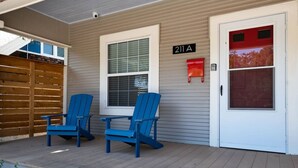 Un porche avec deux fauteuils Adirondack bleus, une boîte aux lettres et une porte portant un numéro.