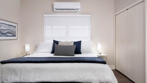Une chambre à coucher comprenant un lit, des lampes de chevet, une fenêtre avec des stores, un appareil de climatisation et une armoire.