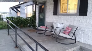 Eine Veranda mit zwei Schaukelstühlen, einem weißen Eimer und einer grünen Tür.