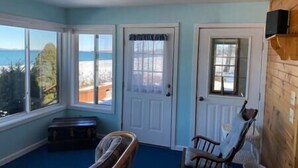 A room with a view of the sea, a wooden bench, a chair, and a door with a window.