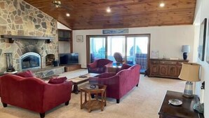 A living room with a stone fireplace, red sofas, a wooden coffee table, and a television.