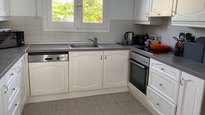 A kitchen with white cabinets, a stainless steel sink, a dishwasher, an oven, and a window with a view of greenery outside. - WATERFRONT VILLA SEAHORSE BAY- HALIKOUNAS (Chalikounas)
