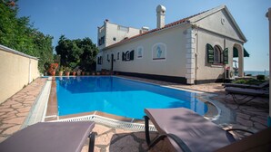 A swimming pool with lounge chairs, a building with arched windows and a tiled roof, and a clear sky. - WATERFRONT VILLA SEAHORSE BAY- HALIKOUNAS (Chalikounas)