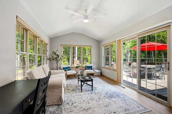 A spacious room with a large window, a ceiling fan, a sofa, a coffee table, and a dining area with outdoor seating.