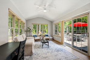A spacious room with a ceiling fan, large windows, a sofa, a coffee table, and a view of an outdoor patio.
