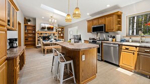 Une cuisine moderne avec des meubles en bois, un îlot central, des tabourets de bar, un four encastré et une grande fenêtre.