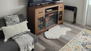 Un salon doté d’un grand téléviseur à écran plat, d’un meuble en bois, d’un canapé gris et d’un tapis aux couleurs vives.