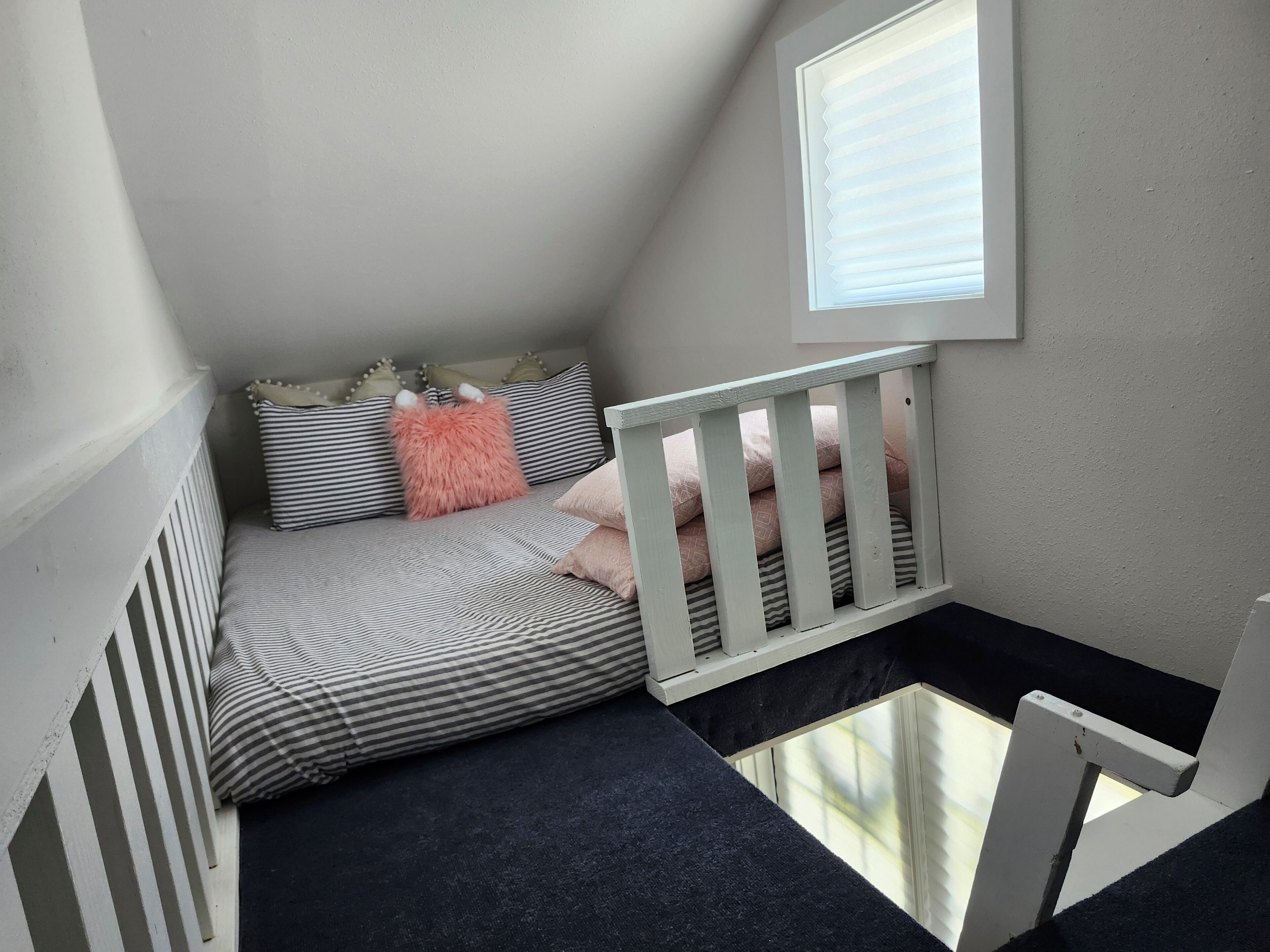 A cozy attic bedroom with a sloped ceiling, a window with blinds, a white crib, and striped bedding.