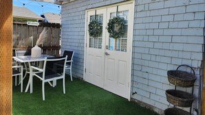 Une terrasse avec une porte blanche, deux couronnes décoratives et une table avec des chaises.
