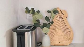 Una cucina con un tostapane, un tagliere di legno e un vaso con foglie verdi.