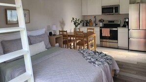 Une chambre avec un lit superposé, un coin repas avec une table et des chaises, et une kitchenette équipée d’un four à micro-ondes, d’un four et d’un réfrigérateur.