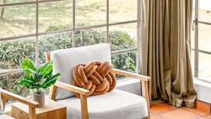 Una habitación acogedora con una silla de madera, una pequeña planta en maceta y una bandeja redonda de madera con objetos encima.