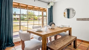 Un comedor con una mesa de madera, sillas, un banco y vistas amplias por las ventanas.