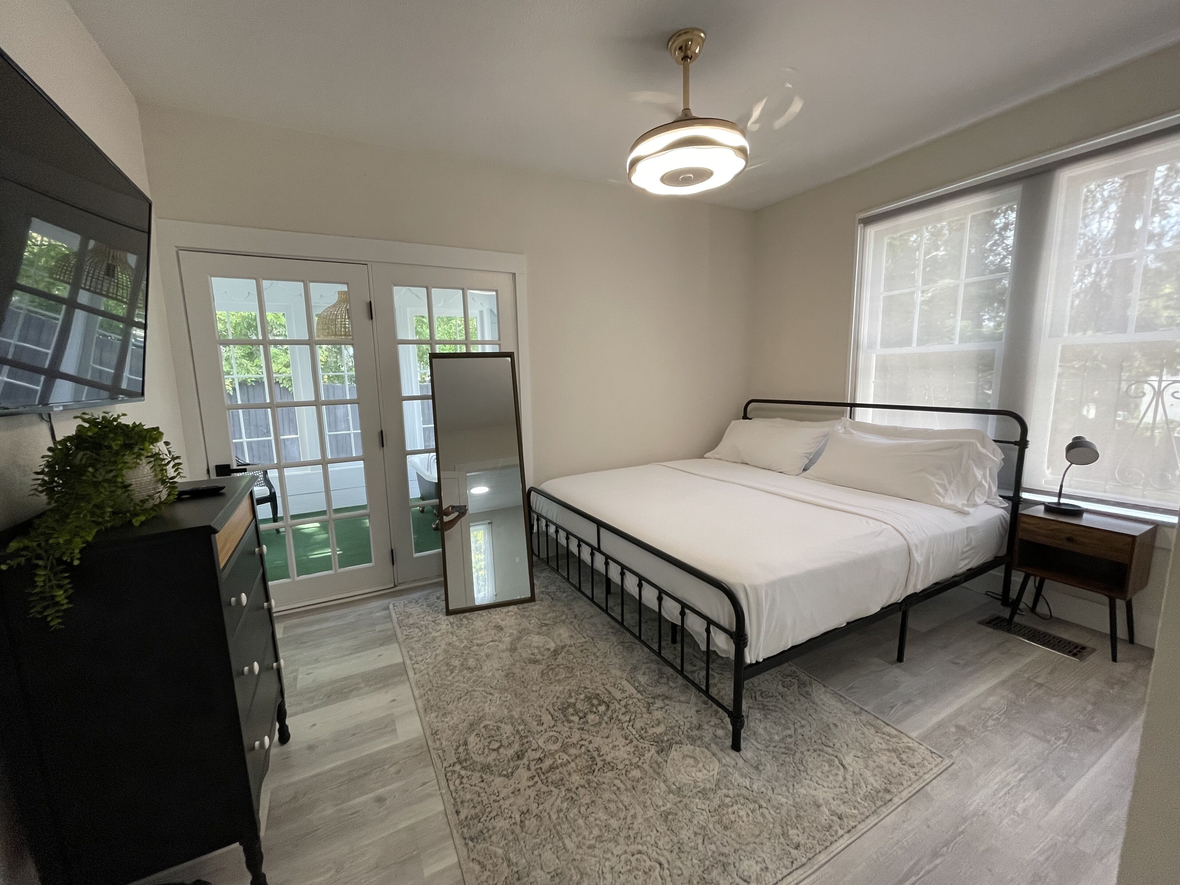 Une chambre à coucher comprenant un lit, une commode, un miroir, une fenêtre et un ventilateur de plafond.