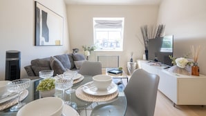 A modern living room with a dining area, a sofa, a TV, and a window with a view. - Newly Renovated 1BDR in Knightsbridge with WiFi (London)