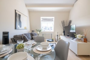 A modern living room with a dining area, a sofa, a TV, and a window with a view. - Newly Renovated 1BDR in Knightsbridge with WiFi (London)