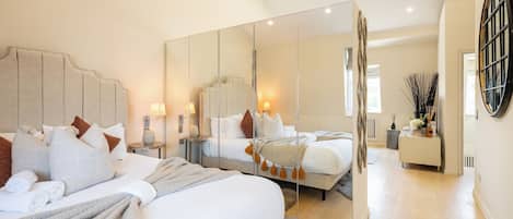 A modern bedroom with a large bed, bedside tables, a mirror, and a view of the adjacent room.