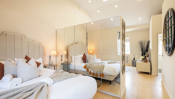 A modern bedroom with a large bed, bedside tables, a mirror, and a view of the adjacent room. - Newly Renovated 1BDR in Knightsbridge with WiFi (London)