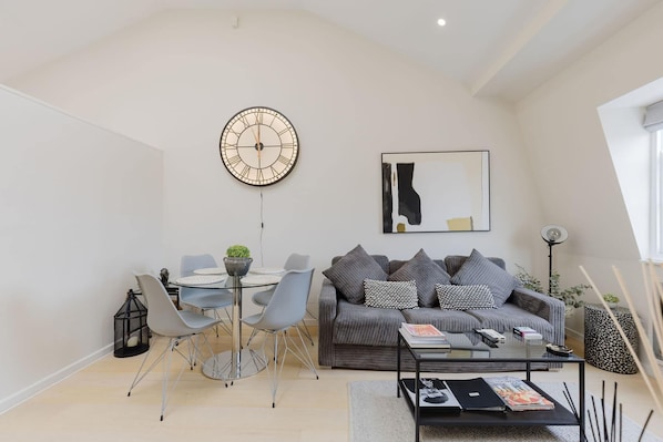 A modern living room with a sofa, coffee table, and a dining area with chairs and a table.