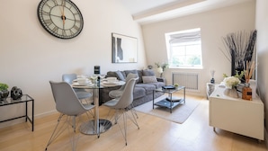 A modern living room with a dining area, a large wall clock, and a window with natural light. - Newly Renovated 1BDR in Knightsbridge with WiFi (London)